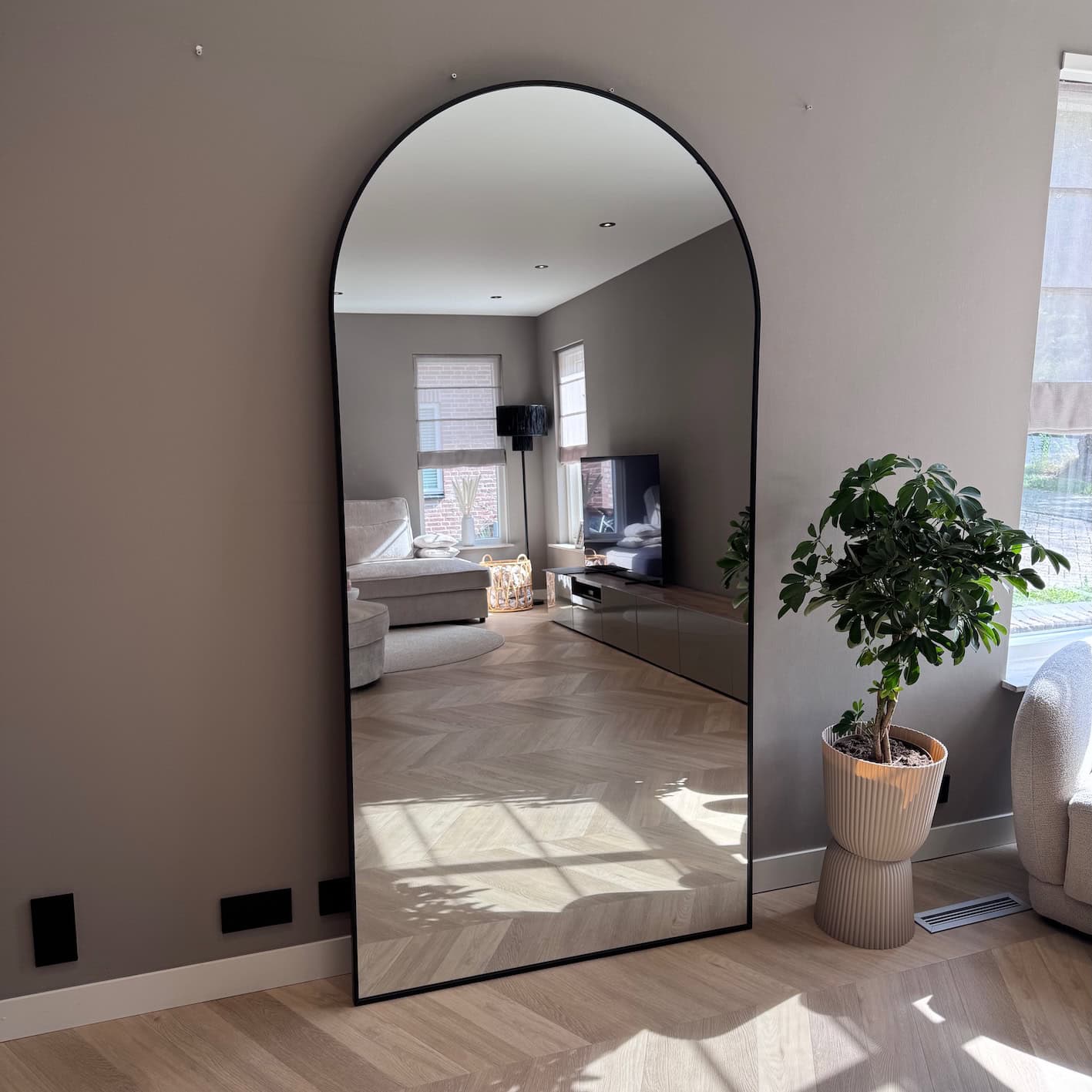 Groot vrijstaand muurspiegel met arkerand voor modern interieur, weerspiegelt woonkamer met comfortabele zitbank, tv en natuurlijke lichtinval. Perfect voor elegant en functioneel huisdecor.