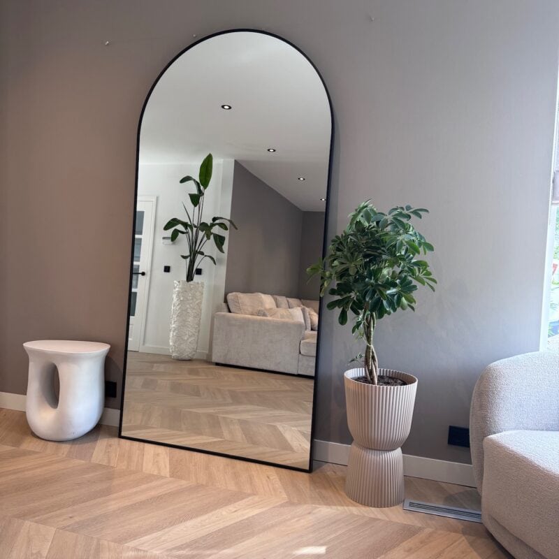 Modern interieur met grote vloerhouten planken en groene planten in stijlvolle potten. Een grote spiegel tilt de ruimte op met natuurlijke lichtinval en minimalistisch design.
