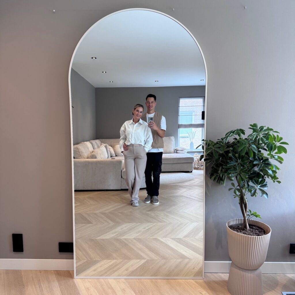 Moderne woonkamer met grote spiegel, comfortabele bank, gezellige sfeer en stijlvolle interieur. Een groene plant voor een frisse uitstraling en natuurlijk licht door raam maakt het geheel compleet.